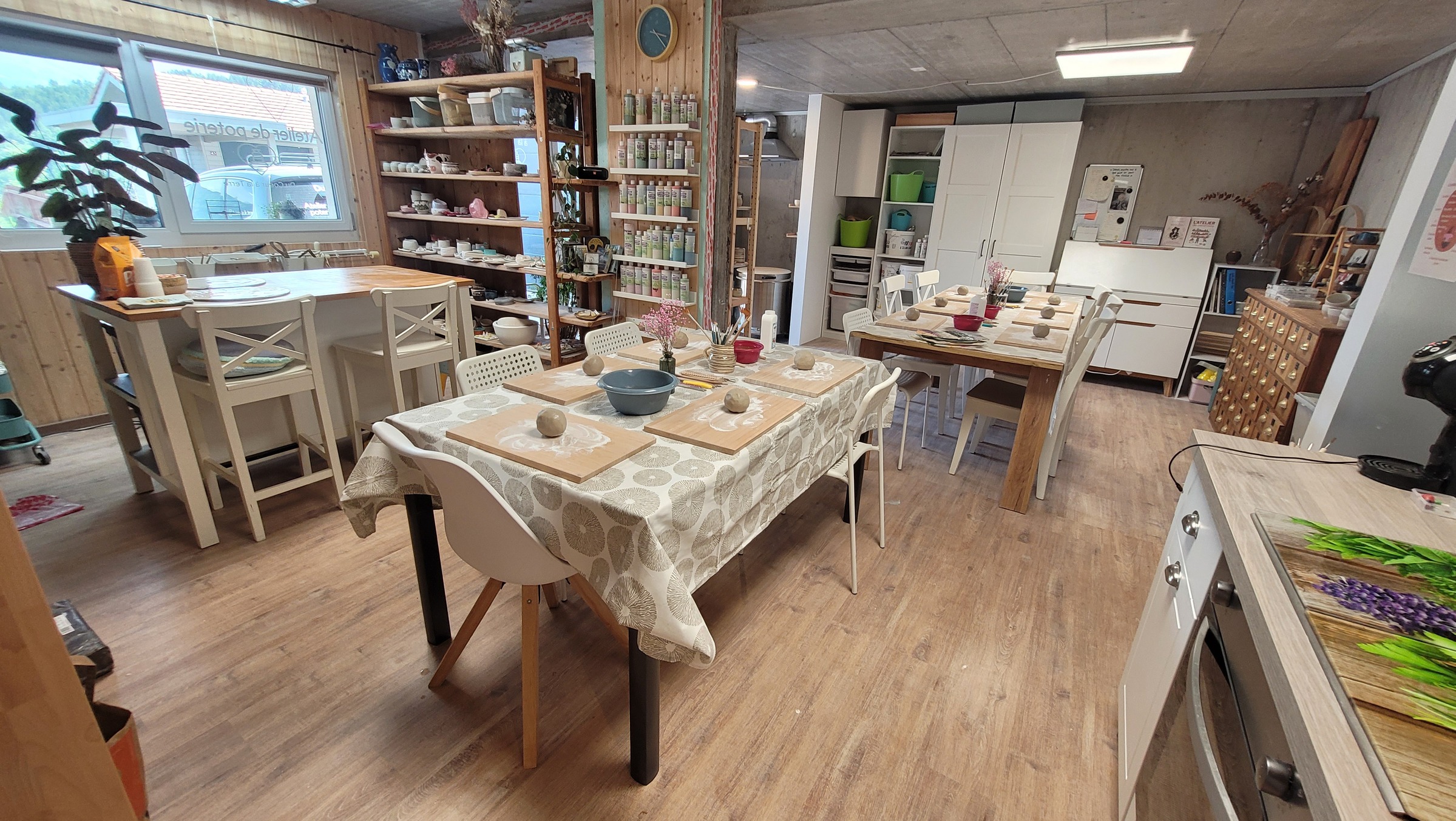 Vue d'ensemble de l'atelier : grandes tables, étagères de pièces et plantes